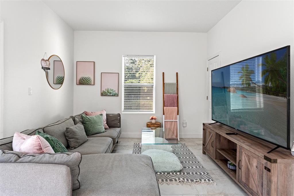 A living room features a grey sectional sofa, a glass coffee table, and a large television — 7911 N PACKWOOD AVENUE, TAMPA, FL