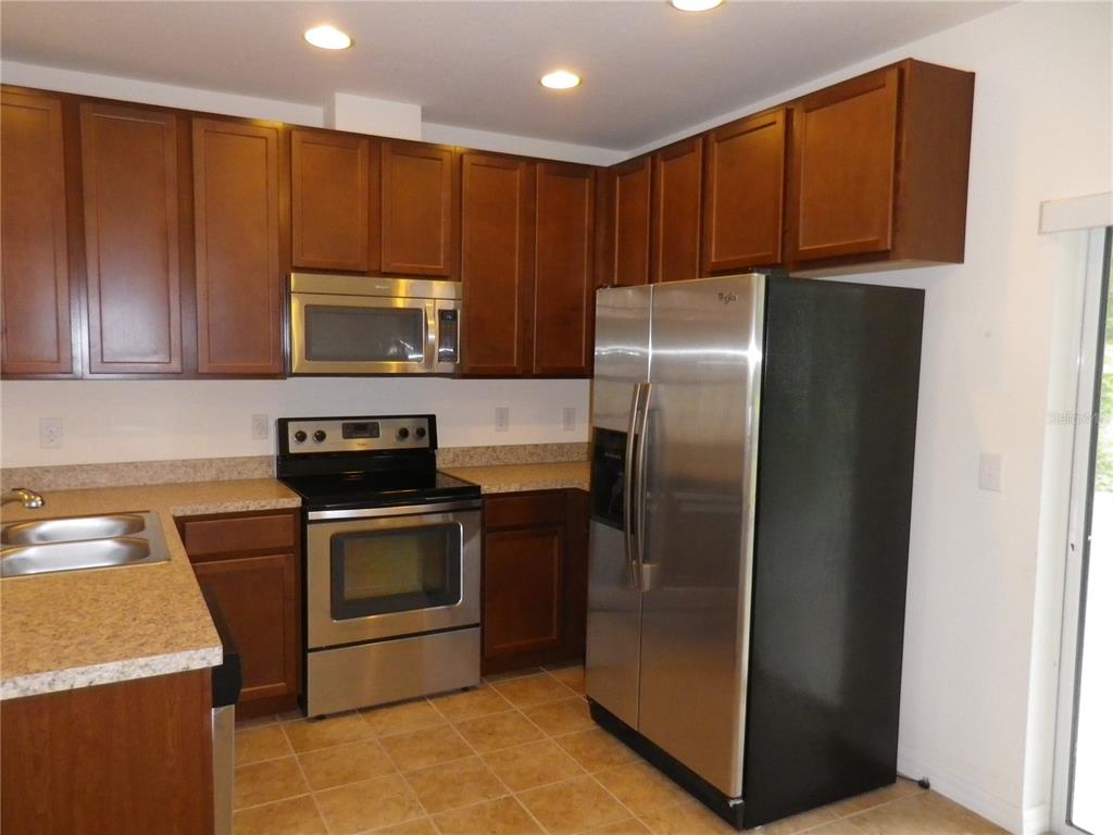 A kitchen with dark wood cabinets, stainless steel appliances, and tan laminate countertops — 15965 FISHHAWK VIEW DRIVE, LITHIA, FL