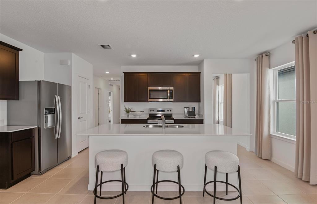 A modern kitchen features dark wood cabinets, a white island with bar seating, and stainless appliances — 5518 FREESIA DRIVE, LAKELAND, FL