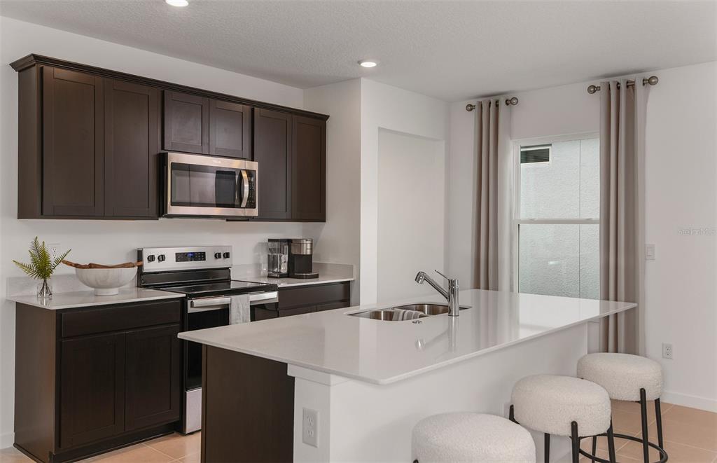 A modern kitchen features dark wood cabinets, white countertops, a center island, and two stools — 5518 FREESIA DRIVE, LAKELAND, FL