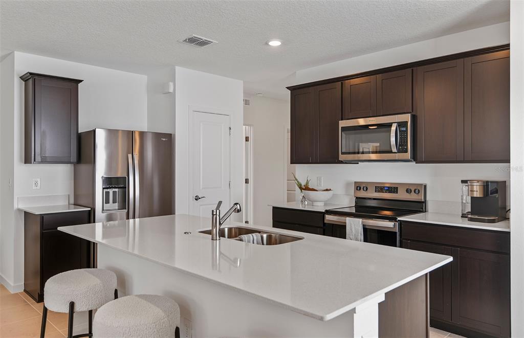 A kitchen features dark wood cabinets, white countertops, a central island, and stainless steel appliances — 5518 FREESIA DRIVE, LAKELAND, FL