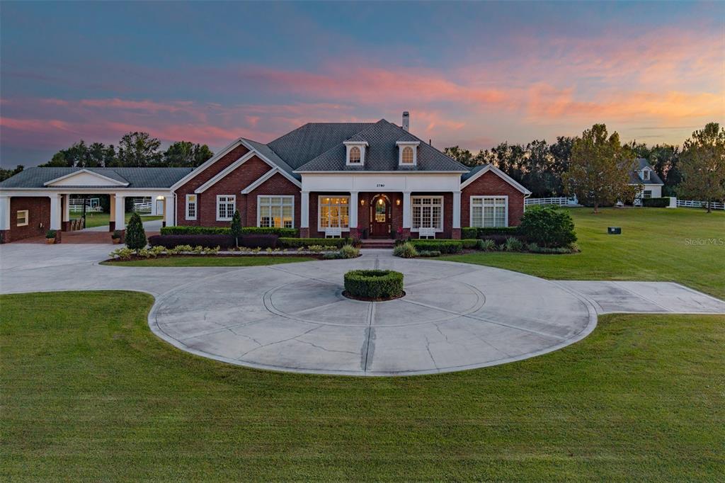 A brick house with a circular driveway and a covered walkway at sunset — 2780 VICKIE COURT, KISSIMMEE, FL