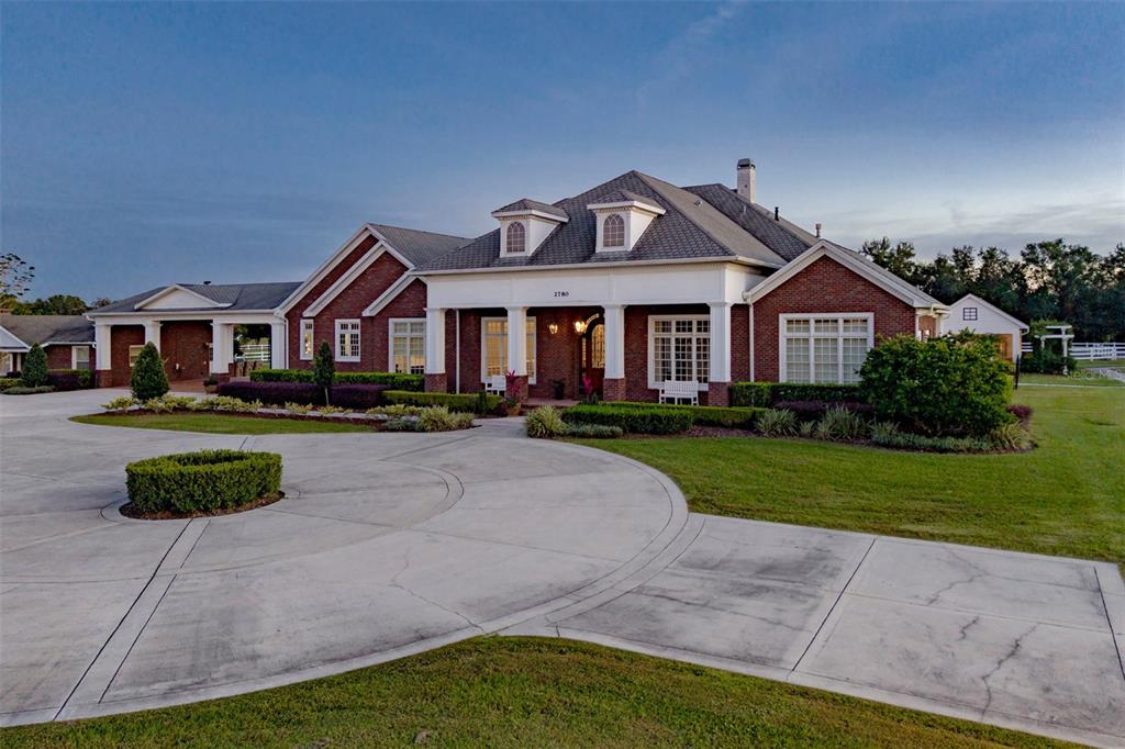 A large brick house with a circular driveway and dormer windows under a blue sky — 2780 VICKIE COURT, KISSIMMEE, FL