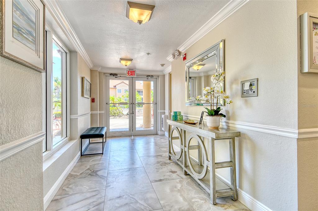 A bright building entryway features tile flooring, a console table, a mirror, and glass doors — 5100 JESSIE HARBOR DRIVE UNIT 504, OSPREY, FL
