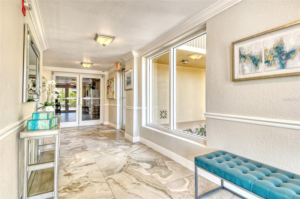 A bright lobby features marble-look tile flooring, a teal tufted bench, and glass entry doors — 5100 JESSIE HARBOR DRIVE UNIT 504, OSPREY, FL