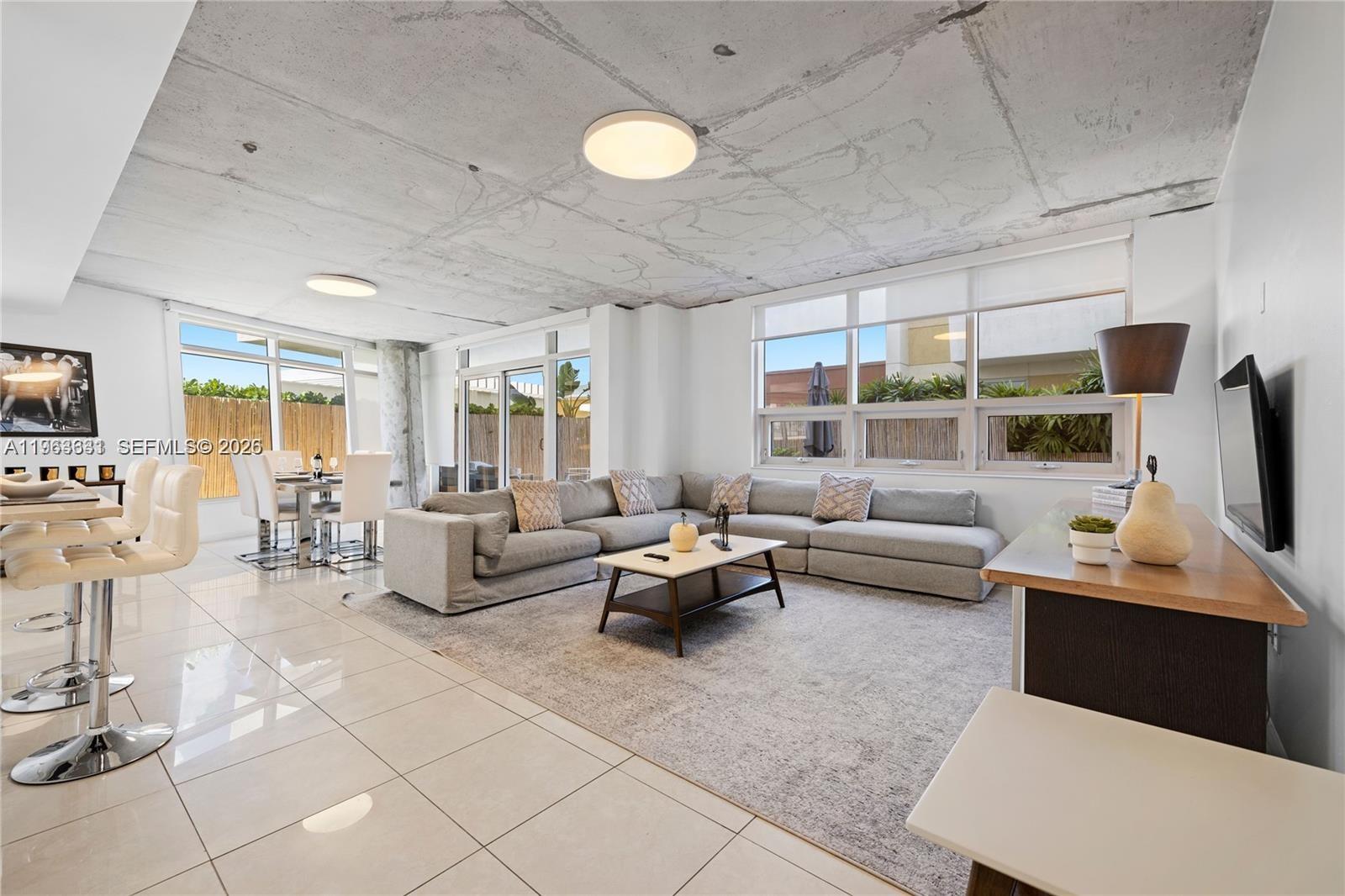 A modern living room features a large gray sectional, tiled floors, and an exposed concrete ceiling — 3250 NE 1st Ave # 515, Miami FL 33137, MIAMI, FL