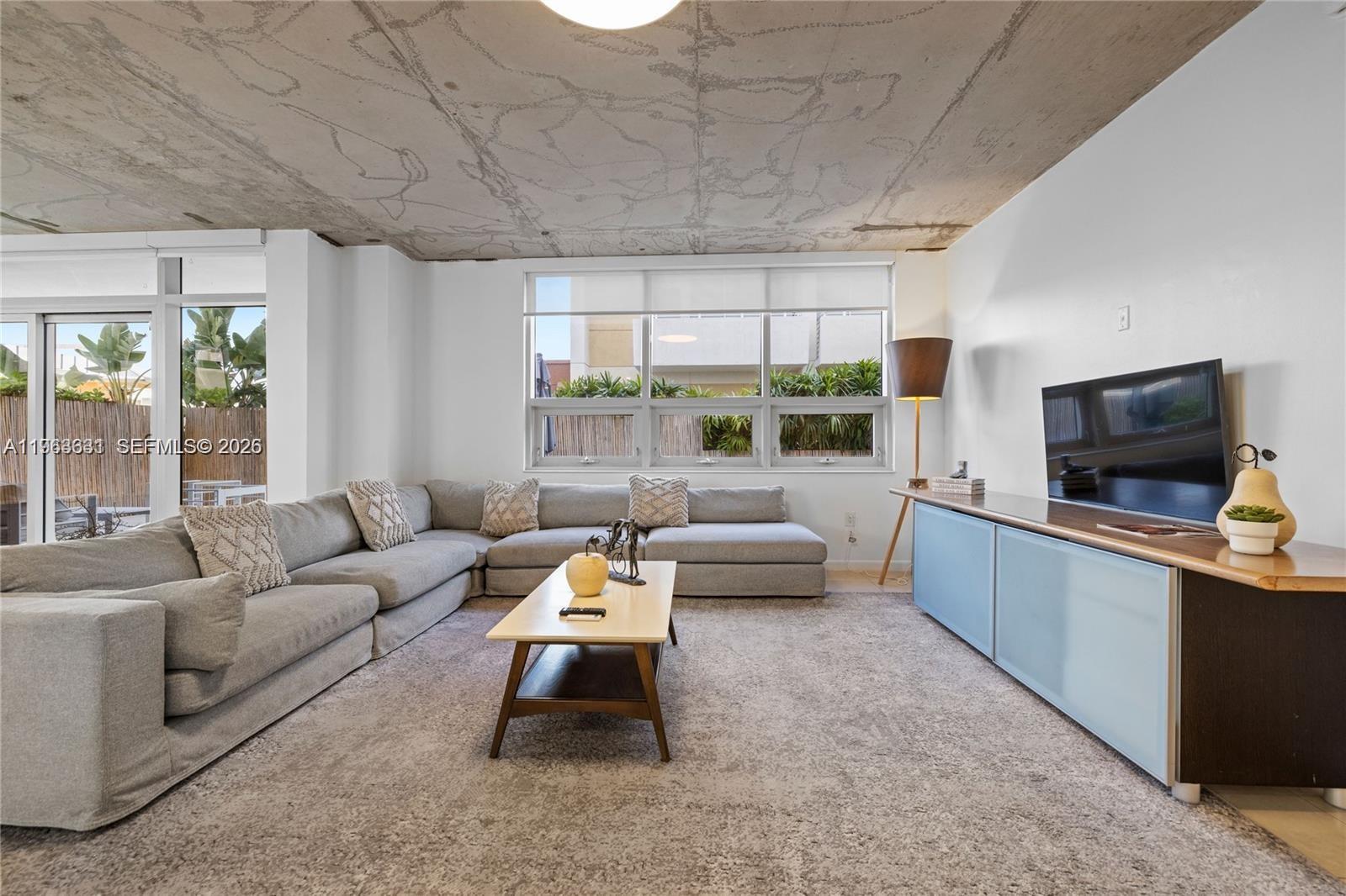 A living room features a large gray sectional sofa, a coffee table, and exposed concrete ceilings — 3250 NE 1st Ave # 515, Miami FL 33137, MIAMI, FL