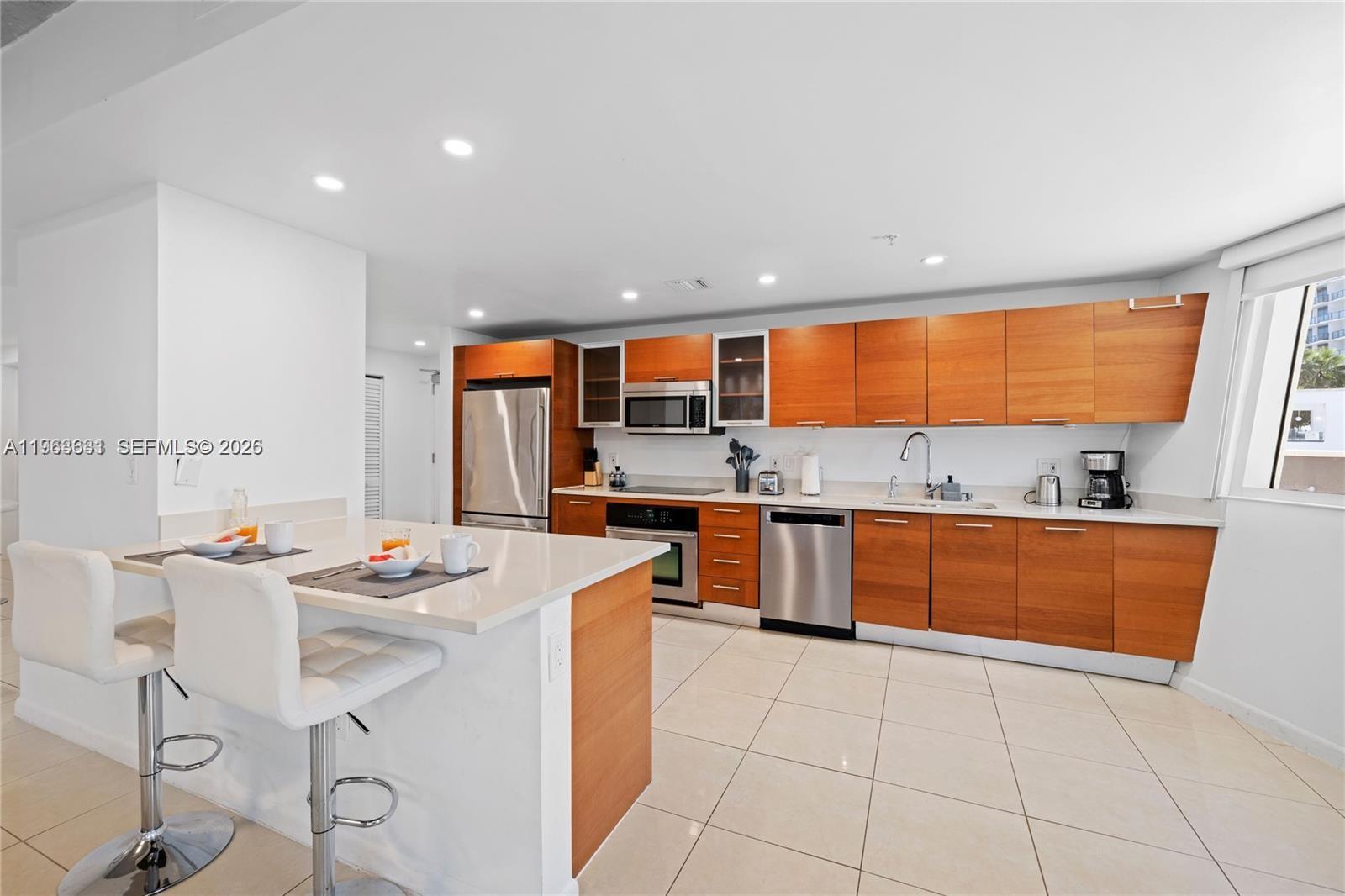 A modern kitchen features wood-toned cabinetry, stainless steel appliances, and a white breakfast bar island — 3250 NE 1st Ave # 515, Miami FL 33137, MIAMI, FL