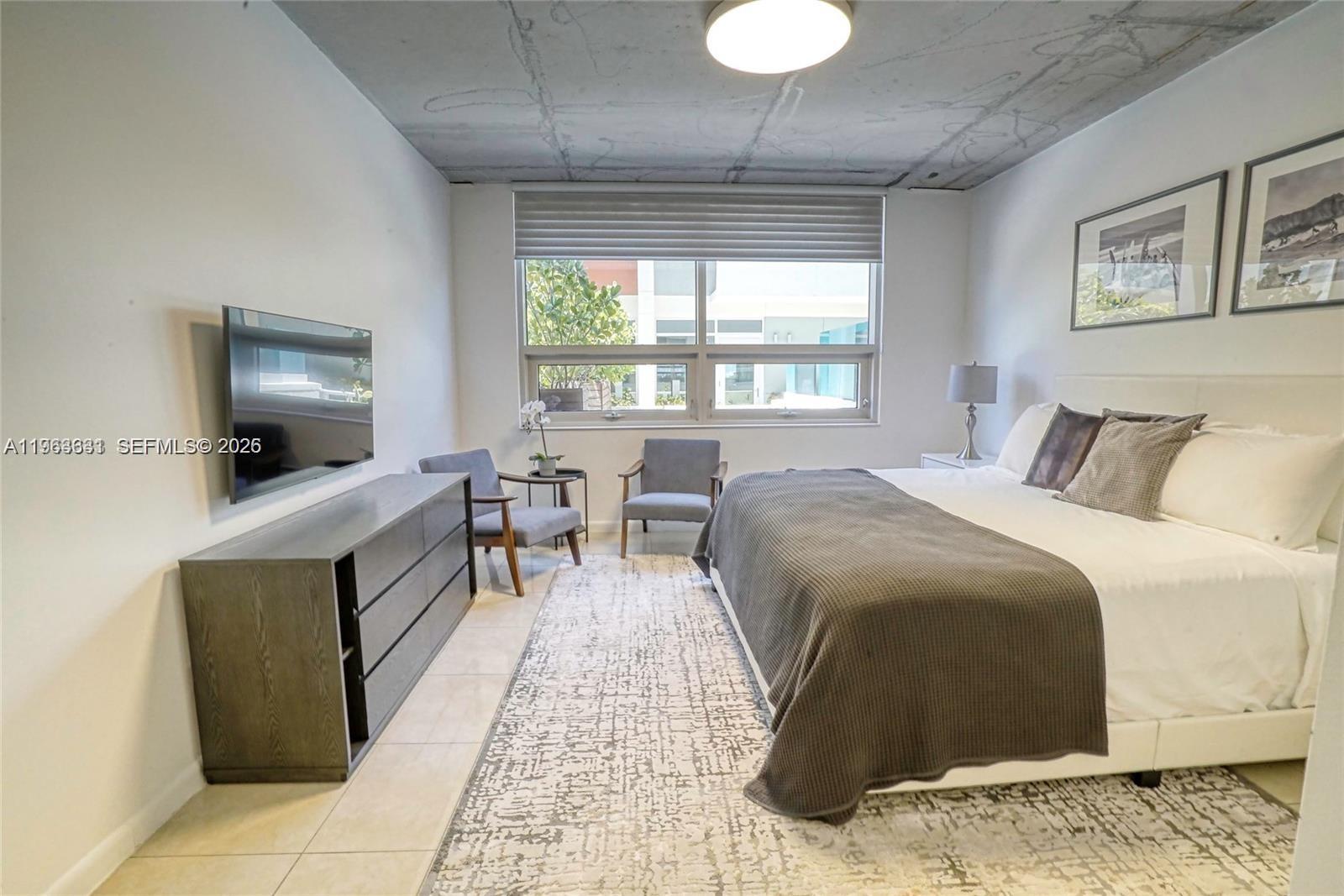 A bedroom features a concrete ceiling, a large bed, a dresser, and two armchairs — 3250 NE 1st Ave # 515, Miami FL 33137, MIAMI, FL