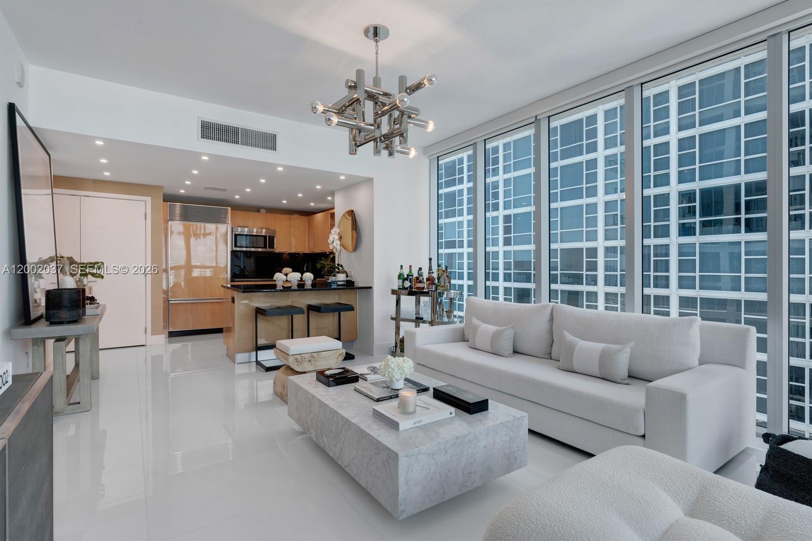 A modern living room features a marble coffee table, white sofa, and an open kitchen — 6899 Collins Ave # 1109, Miami Beach FL 33141, MIAMI BEACH, FL
