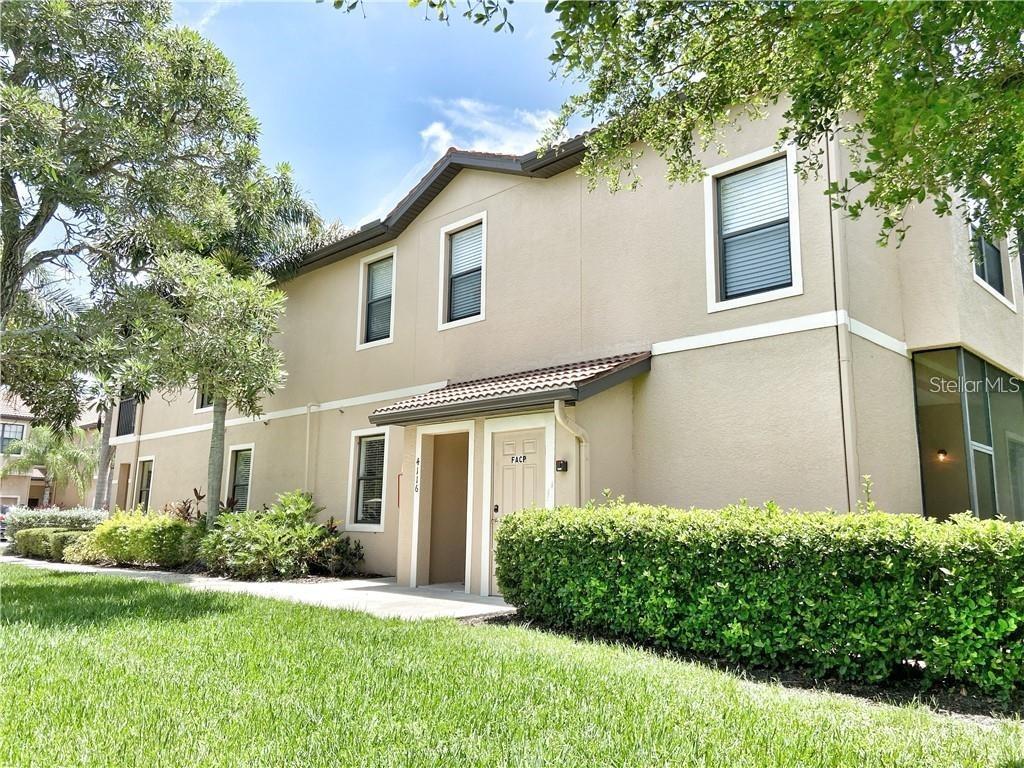 A two-story tan stucco building with a tiled entryway and a manicured hedge in front — 4114 VIA PIEDRA CIRCLE UNIT 1-104, SARASOTA, FL