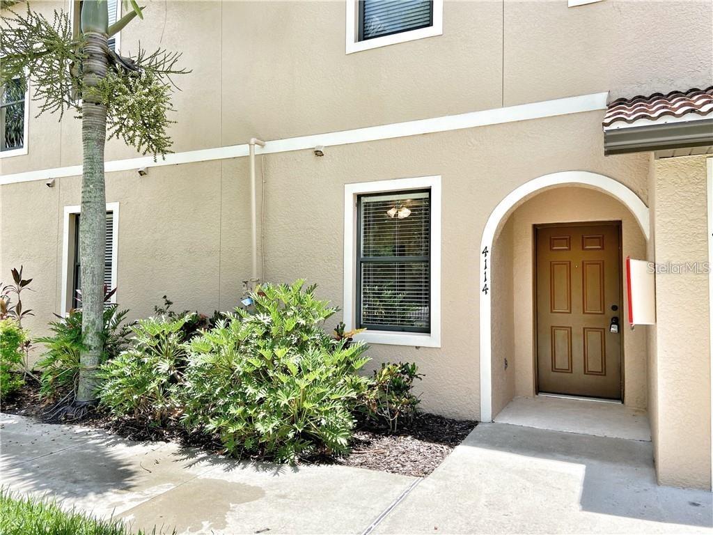 The exterior of a tan stucco building features a brown front door and landscaping — 4114 VIA PIEDRA CIRCLE UNIT 1-104, SARASOTA, FL
