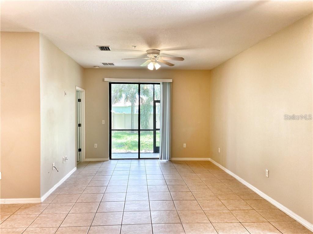 An empty living room features beige walls, tile flooring, a ceiling fan, and sliding glass doors — 4114 VIA PIEDRA CIRCLE UNIT 1-104, SARASOTA, FL