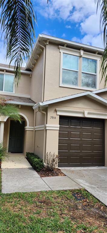 A two-story tan townhouse features a brown garage door, a front entrance, and palm fronds — 2914 ROYAL TUSCAN LANE, VALRICO, FL