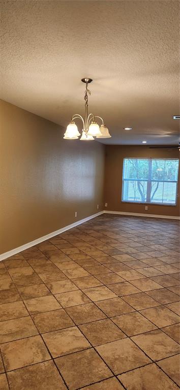 An empty room features tan walls, a chandelier, and brown square tile flooring — 2914 ROYAL TUSCAN LANE, VALRICO, FL