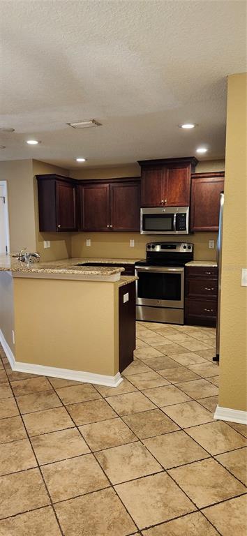 A kitchen features dark wood cabinets, stainless steel appliances, granite countertops, and beige tile flooring — 2914 ROYAL TUSCAN LANE, VALRICO, FL