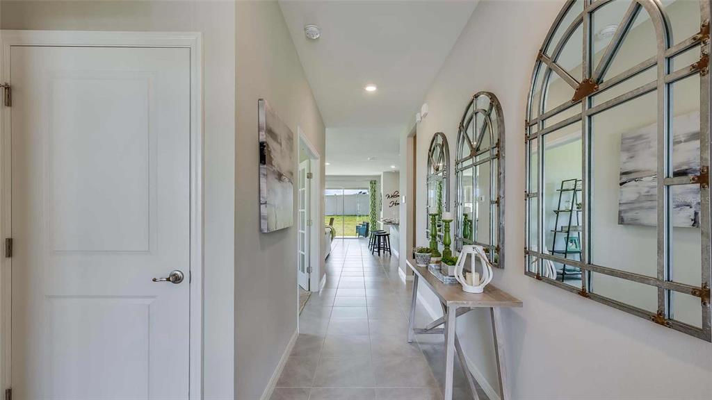 A hallway features tile flooring, a console table with mirrors, and a view toward a backyard — 17295 SALTBUSH TRAIL, PARRISH, FL