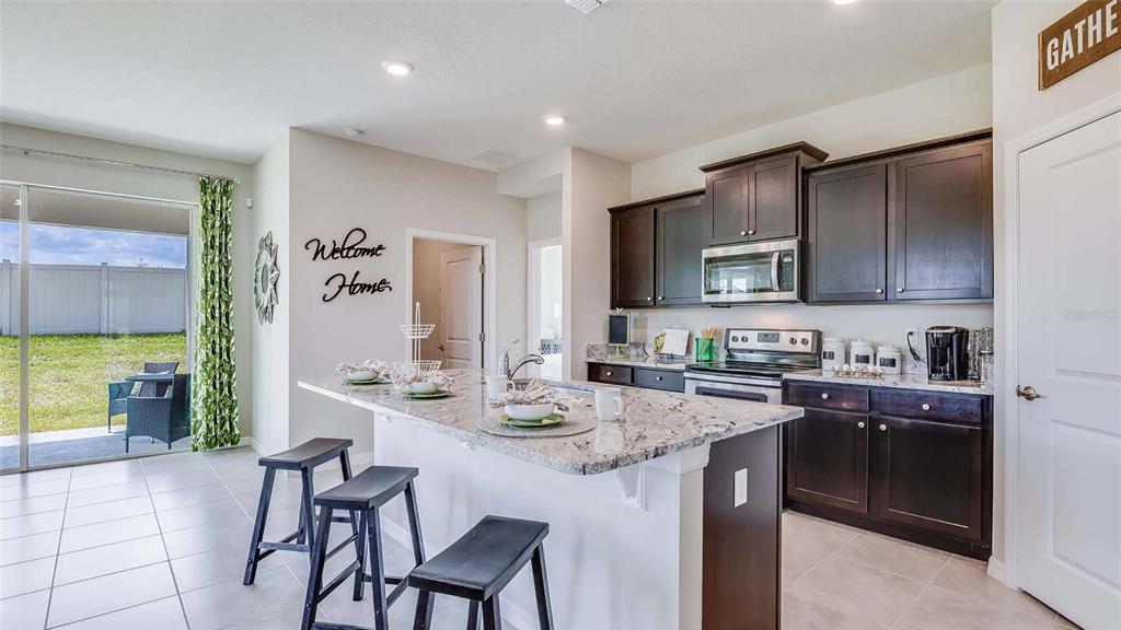 A kitchen features dark wood cabinets, granite countertops, a center island, and tile flooring — 17295 SALTBUSH TRAIL, PARRISH, FL