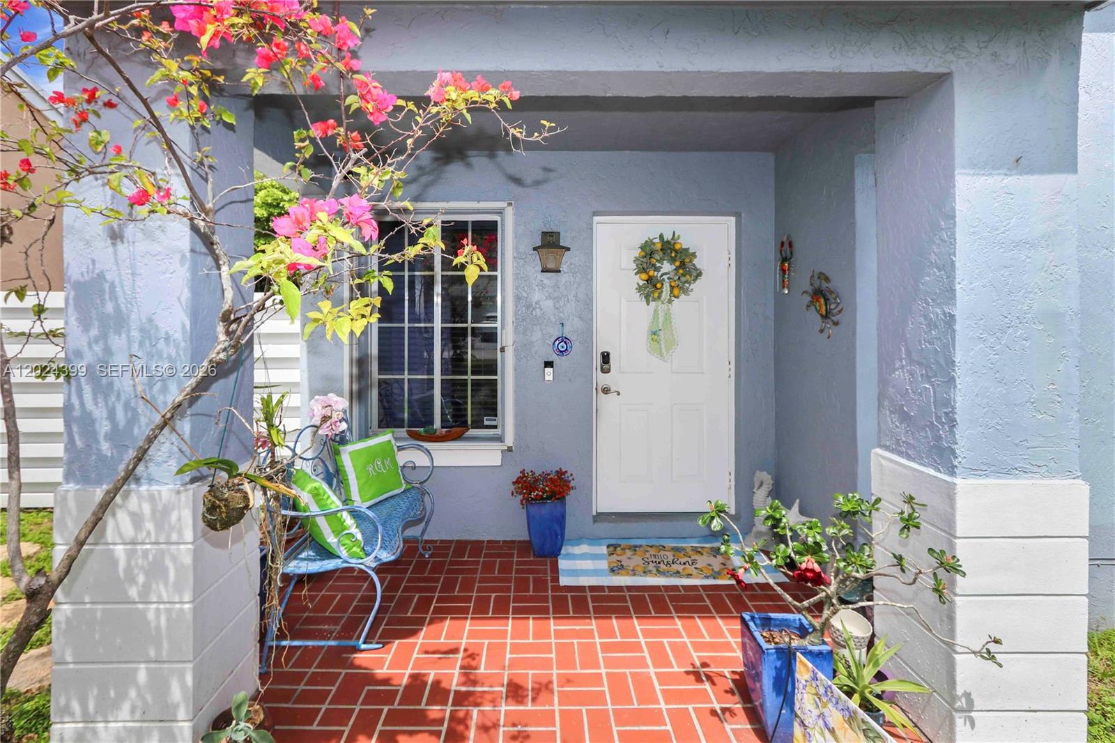 A covered front porch features a white door, a blue bench, and red brick flooring — 14454 SW 138th Ct, Miami FL 33186, MIAMI, FL