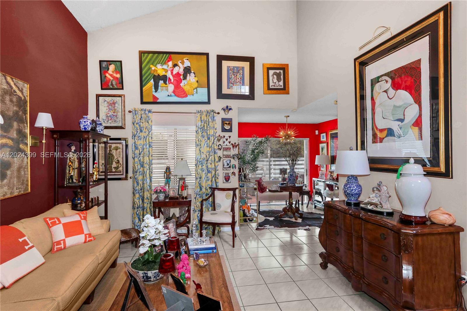 A living room features vaulted ceilings, tiled floors, a red accent wall, and eclectic artwork — 14454 SW 138th Ct, Miami FL 33186, MIAMI, FL