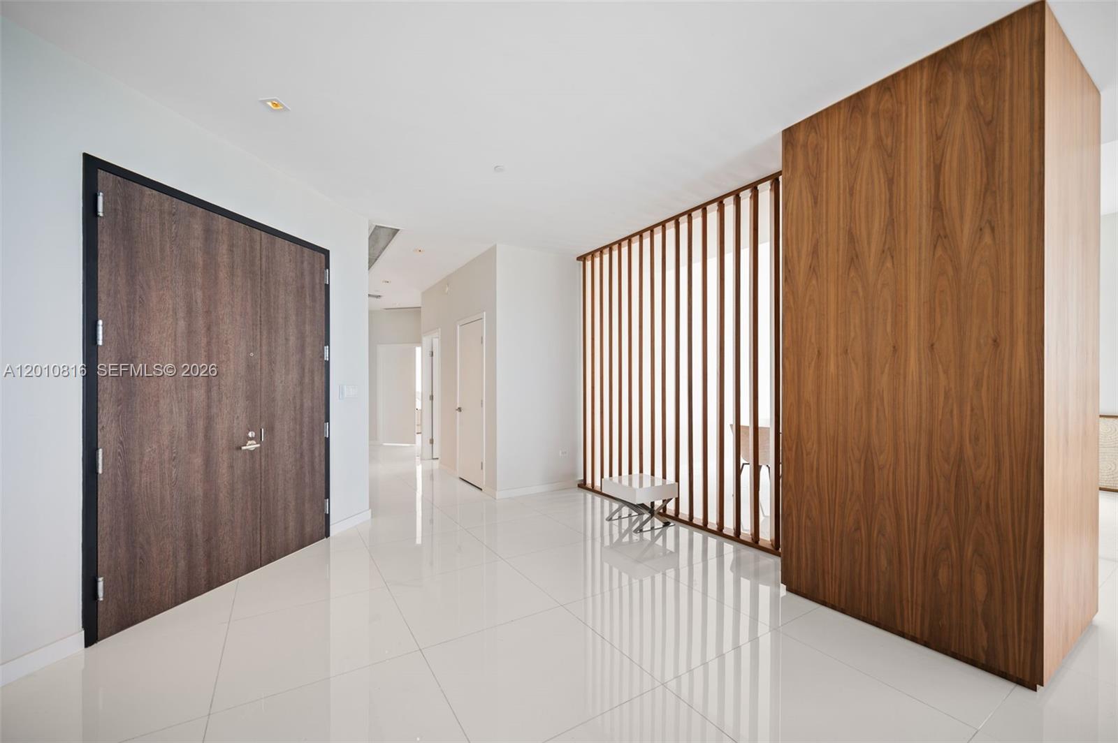 A modern entryway features white tile floors, a wooden accent wall, and a slatted room divider — 88 SW 7th St, Miami FL 33130, MIAMI, FL