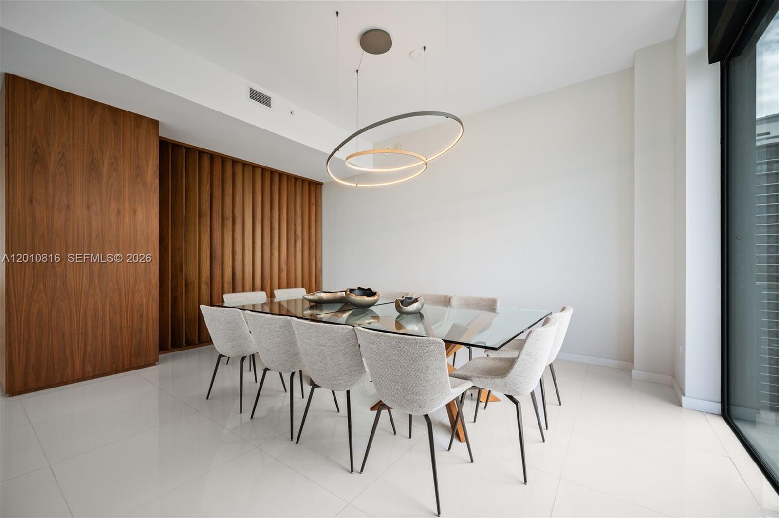 A dining room features a glass-topped table, upholstered chairs, a modern pendant light, and wood-paneled walls — 88 SW 7th St, Miami FL 33130, MIAMI, FL