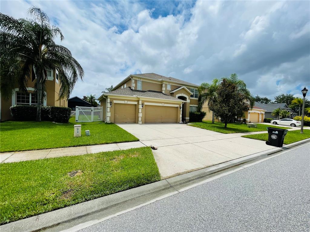A two-story suburban house with a tan exterior, a three-car garage, and a concrete driveway — 1418 SPRING FEST LANE, ORLANDO, FL