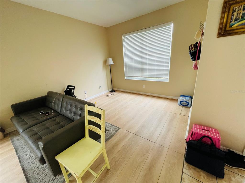 A living room features light wood-look flooring, a dark gray sofa, and a yellow chair — 1418 SPRING FEST LANE, ORLANDO, FL