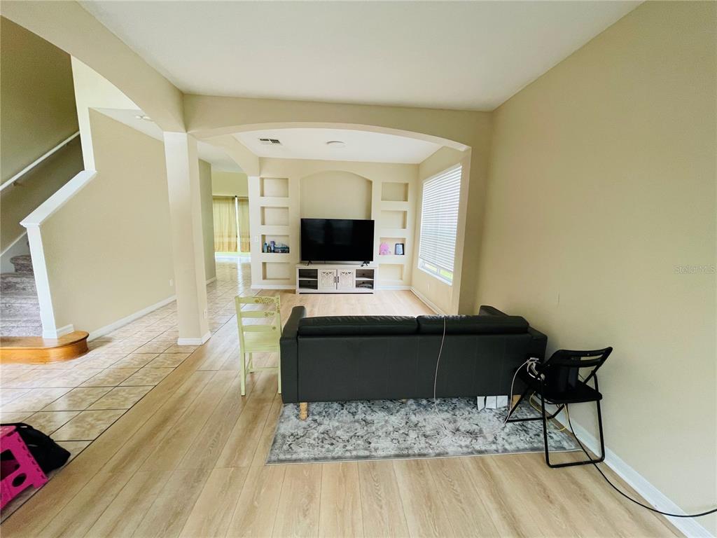 A living room features light wood-look flooring, a black sofa, and built-in wall niches — 1418 SPRING FEST LANE, ORLANDO, FL