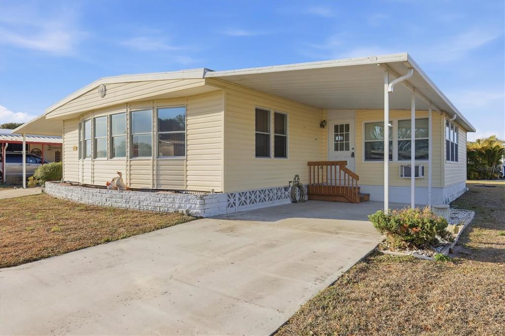 A light yellow mobile home with a concrete driveway, carport, and white brick skirting — 6710 36TH AVENUE E UNIT 201, PALMETTO, FL