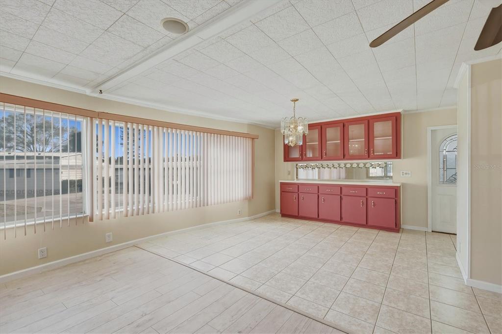 A dining room features red cabinetry, a chandelier, tile flooring, and large vertical blinds — 6710 36TH AVENUE E UNIT 201, PALMETTO, FL