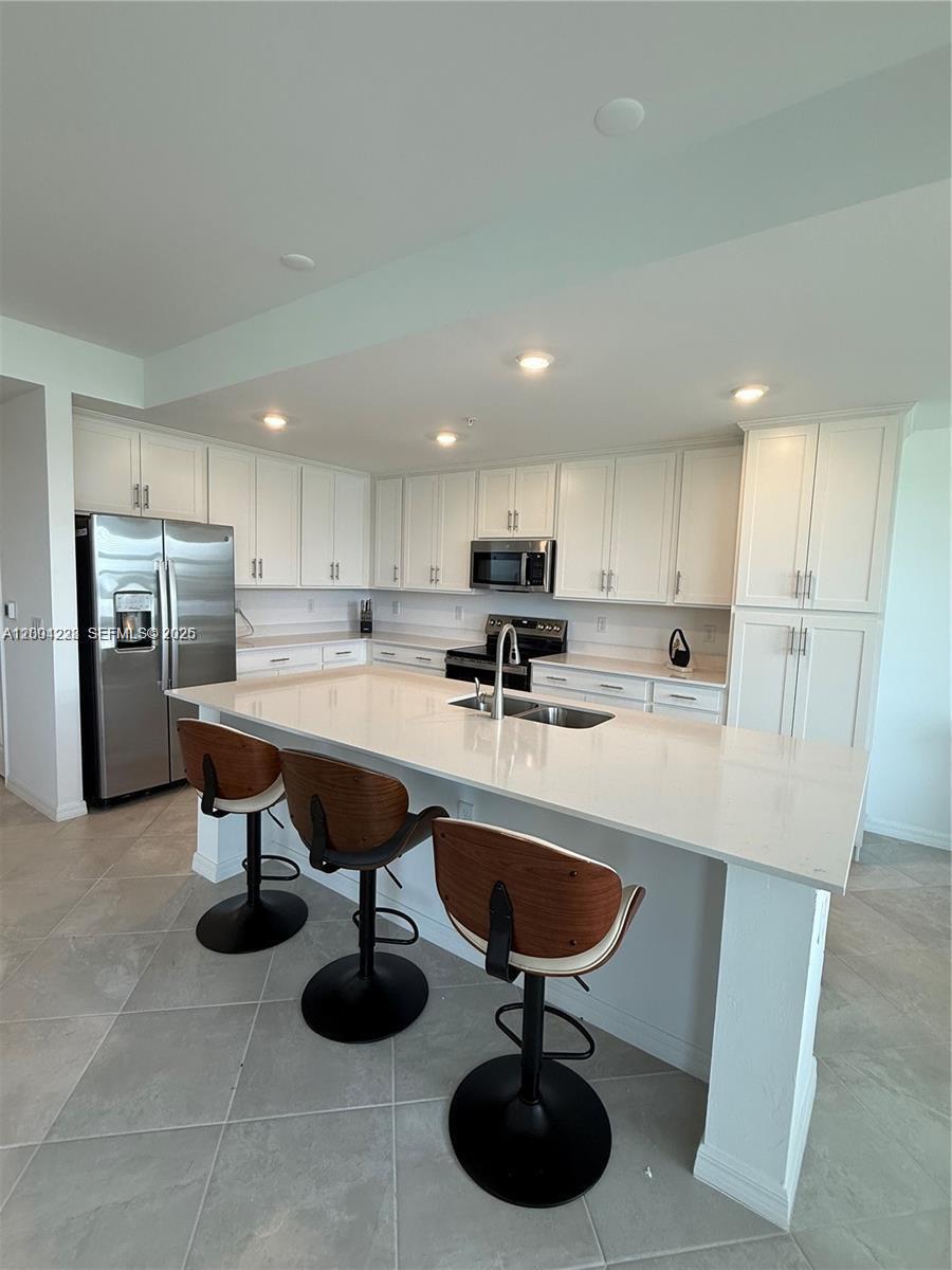 A modern kitchen features white cabinetry, a large quartz island, and three wooden bar stools — 5555 Double Eager Circle # 3917, Ave Maria FL 34142, AVE MARIA, FL