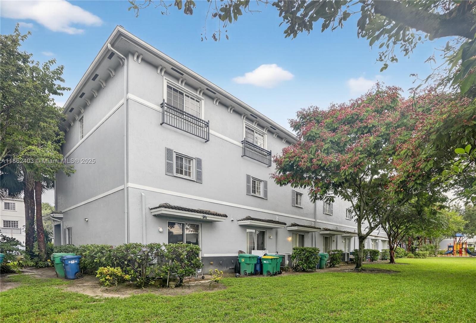 The exterior of a three-story gray townhouse building features multiple sliding glass doors and trash bins — 3445 NW 14th Ct, Lauderhill FL 33311, LAUDERHILL, FL