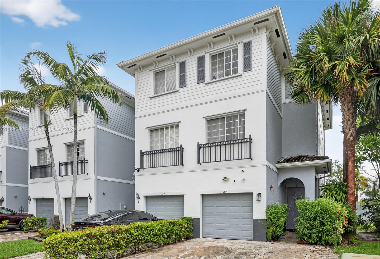 A three-story white townhouse with two garage doors and a small front garden — 3445 NW 14th Ct, Lauderhill FL 33311, LAUDERHILL, FL