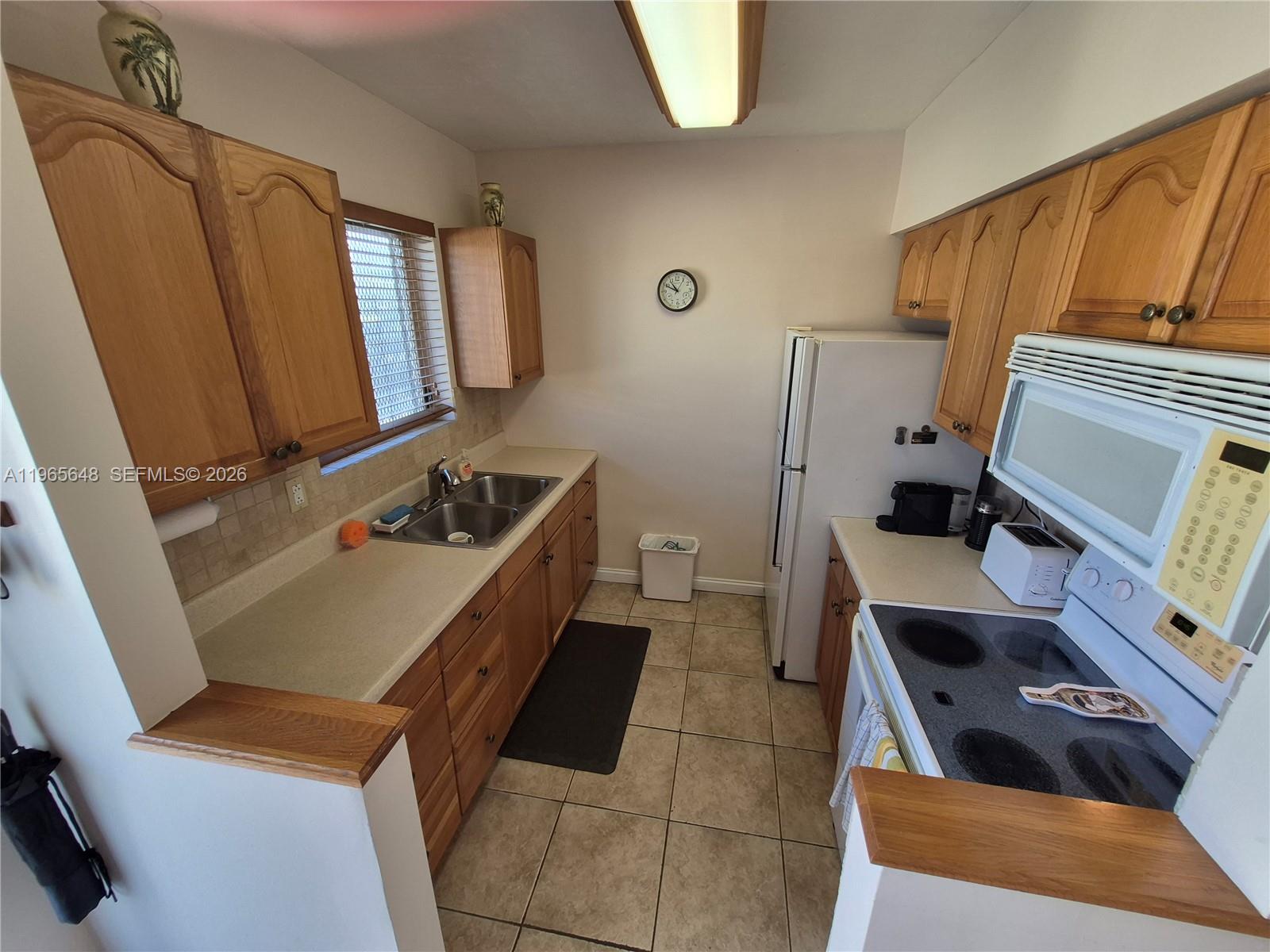 A galley kitchen features oak cabinets, light countertops, tile flooring, and white appliances — 520 Euclid Ave # 8, Miami Beach FL 33139, MIAMI BEACH, FL