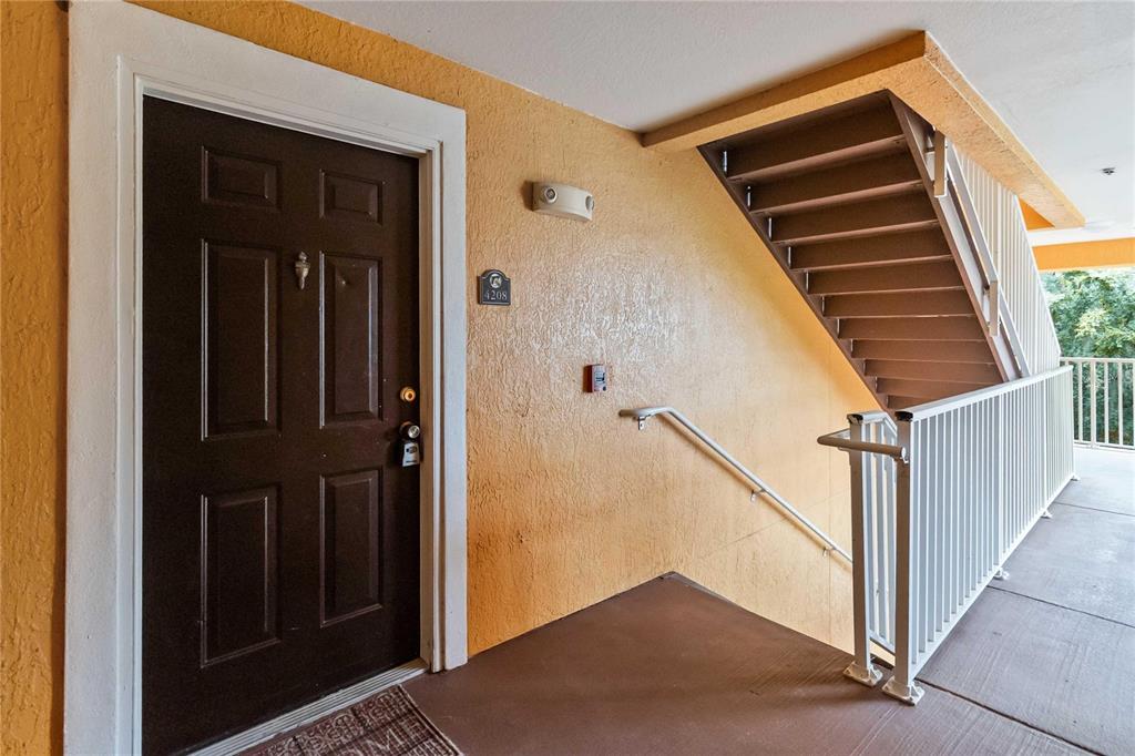 A dark brown front door with a number plate sits beside an outdoor staircase — 5459 VINELAND RD UNIT 4208, ORLANDO, FL
