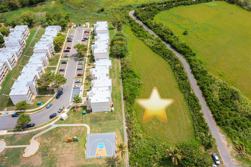 An aerial view shows a residential complex next to an undeveloped grassy lot with a star — CARR 485 KM 1.7 BO. MEMBRILLO, CAMUY, PR