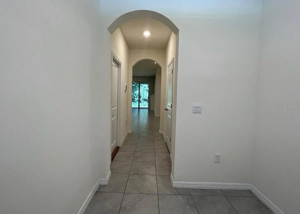 A hallway with arched entryways, white walls, and light-colored tile flooring leads to a doorway — 32867 PEZ LANDING LANE, WESLEY CHAPEL, FL