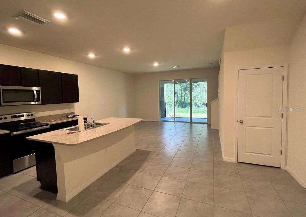 A kitchen with dark cabinets and a granite island opens to a tiled living area — 32867 PEZ LANDING LANE, WESLEY CHAPEL, FL