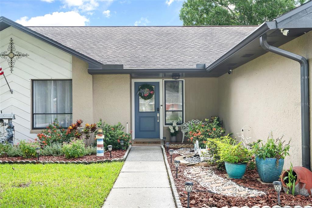 The exterior of a single-story home features a blue front door and landscaped front yard — 15747 SCRIMSHAW DRIVE, TAMPA, FL