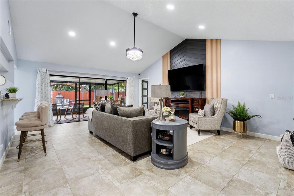 A living room features a vaulted ceiling, a gray sofa, and a television mounted on wood — 15747 SCRIMSHAW DRIVE, TAMPA, FL