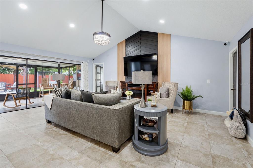 A living room features a vaulted ceiling, a gray sofa, and a wood-paneled accent wall — 15747 SCRIMSHAW DRIVE, TAMPA, FL