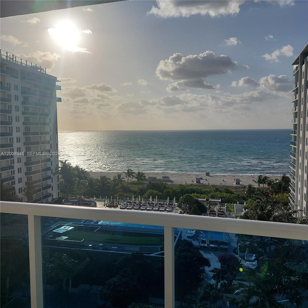A balcony view overlooks a swimming pool, sandy beach, and the ocean between two buildings — 2301 Collins Ave # 1125, Miami Beach FL 33139, MIAMI BEACH, FL