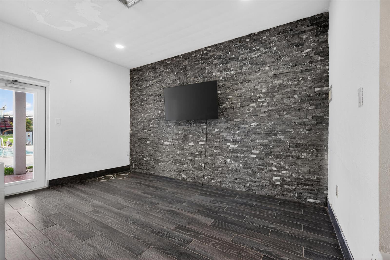 A room features dark wood-look tile flooring, white walls, and a dark stone accent wall — 360 Kismet Avenue, Pahokee FL 33476, PAHOKEE, FL