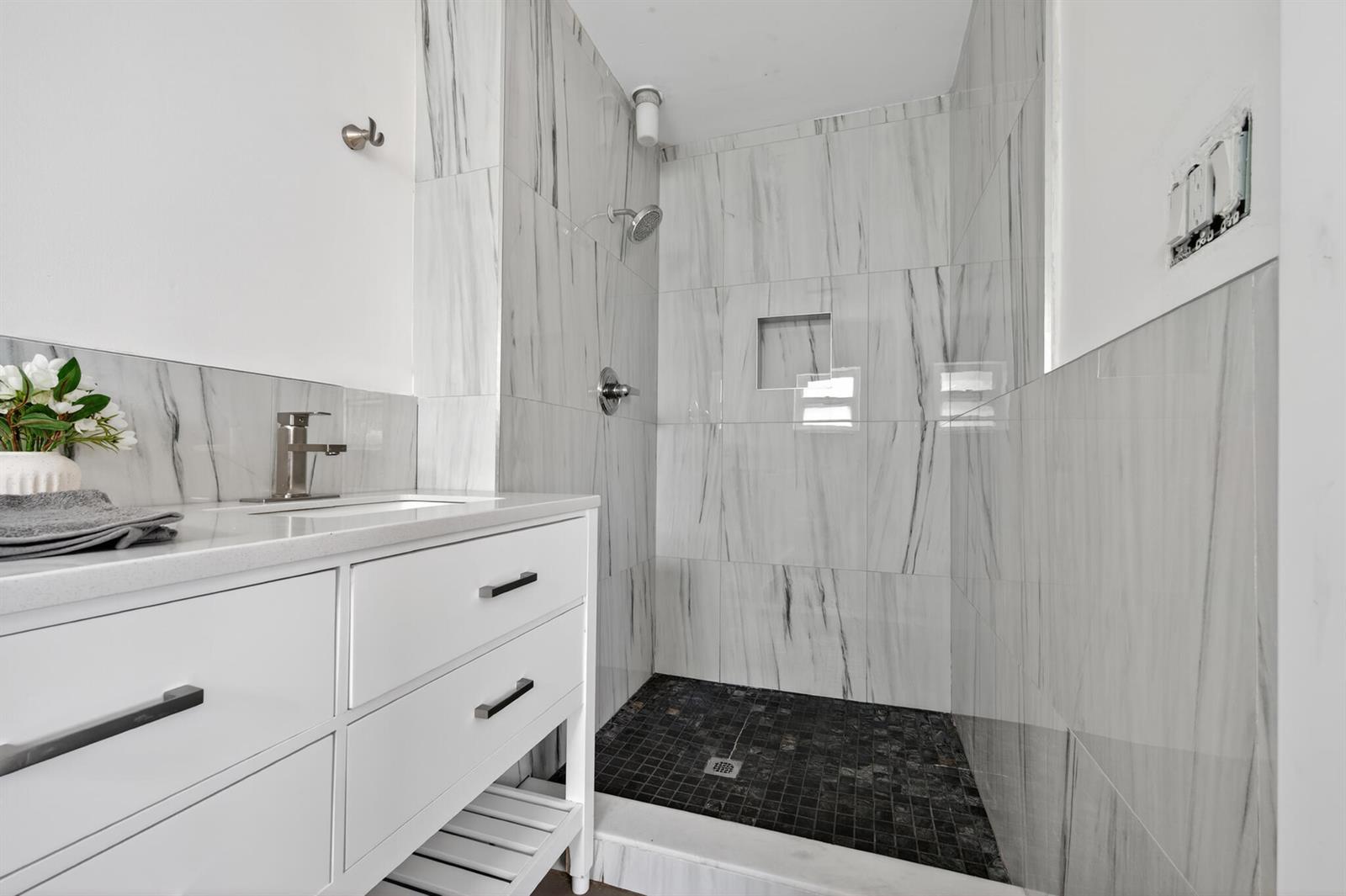 A bathroom features a white vanity, marble-look wall tiles, and a dark tiled shower floor — 360 Kismet Avenue, Pahokee FL 33476, PAHOKEE, FL