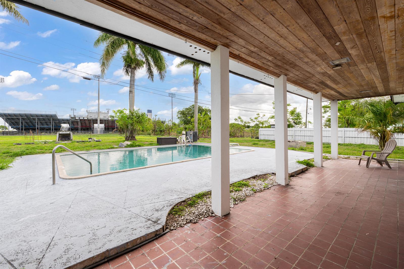 A covered patio with tiled flooring overlooks a swimming pool and a nearby stadium — 360 Kismet Avenue, Pahokee FL 33476, PAHOKEE, FL