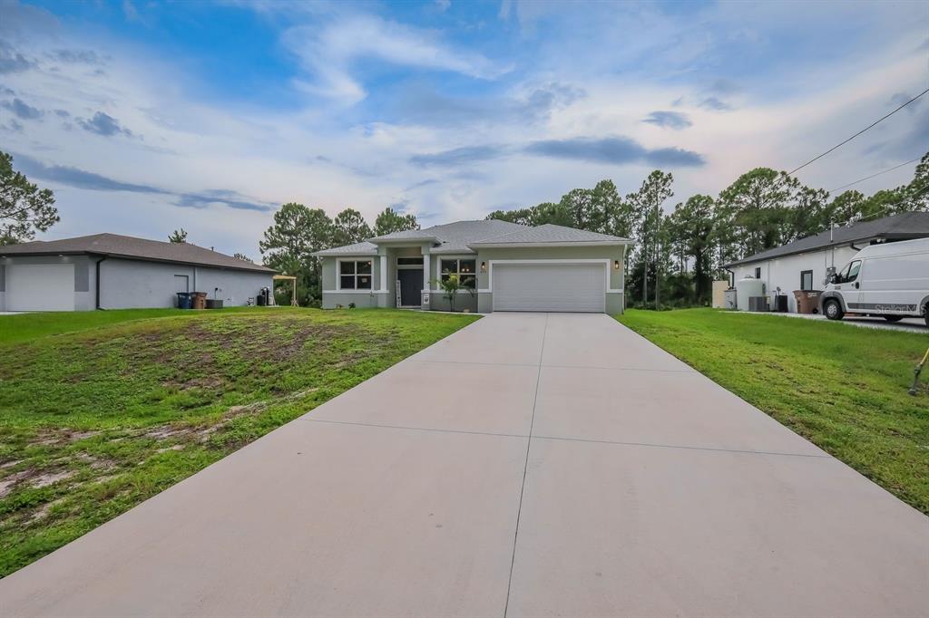 A single-story house with a light green exterior, a two-car garage, and a concrete driveway — 670 NIMITZ BOULEVARD, LEHIGH ACRES, FL