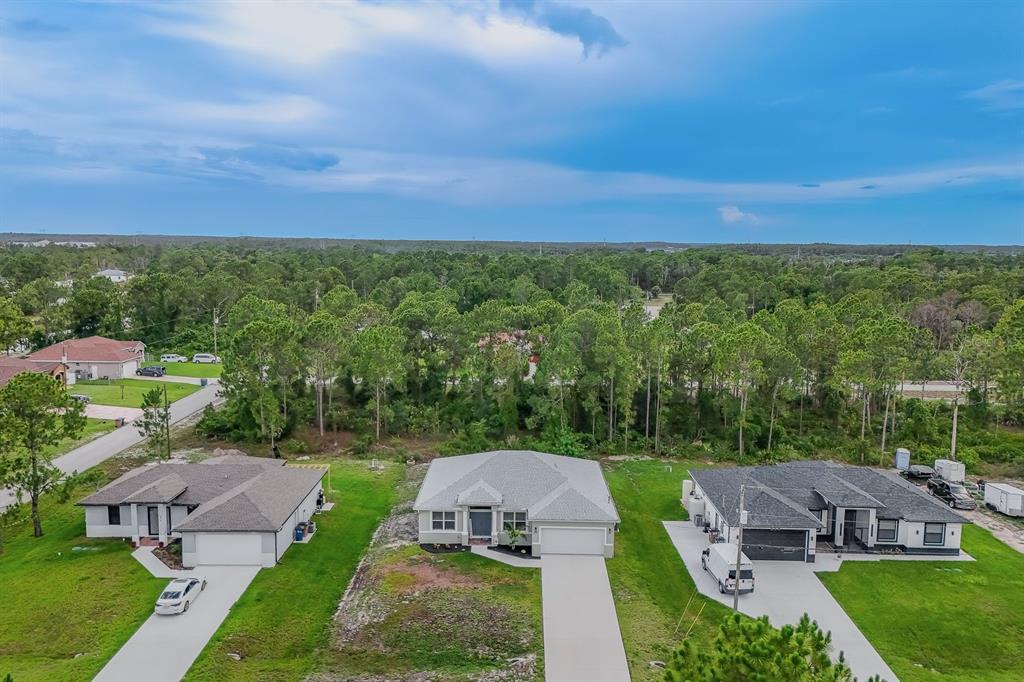 An aerial view shows three suburban houses surrounded by a dense forest under a cloudy sky — 670 NIMITZ BOULEVARD, LEHIGH ACRES, FL