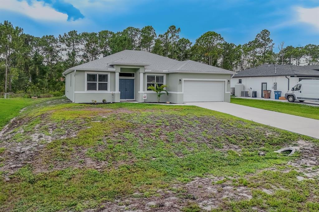 A single-story house with a light green exterior, a two-car garage, and a concrete driveway — 670 NIMITZ BOULEVARD, LEHIGH ACRES, FL