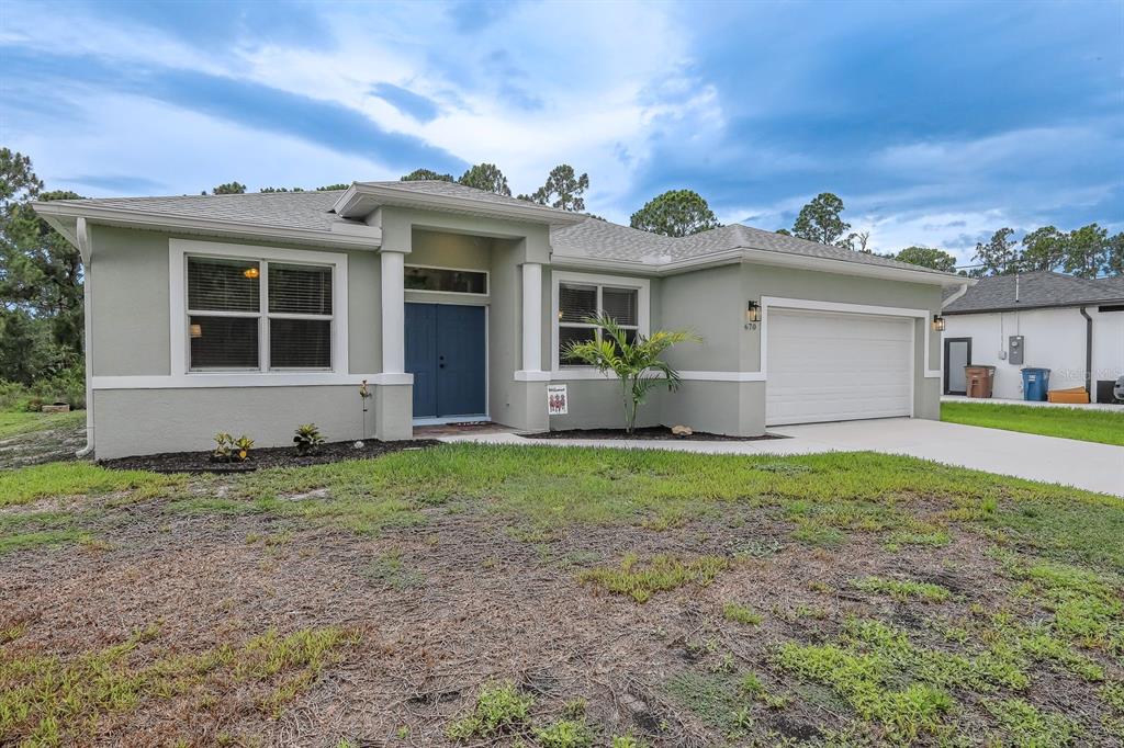 A single-story house with light green stucco siding, a two-car garage, and blue double doors — 670 NIMITZ BOULEVARD, LEHIGH ACRES, FL